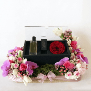 orchids, roses and hydrangea surrounding a box of revealing red perfume with oud and rose amor rose